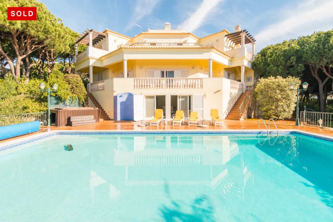 A yellow two-story house with a pool in front and a "SOLD" sign in the upper left corner.