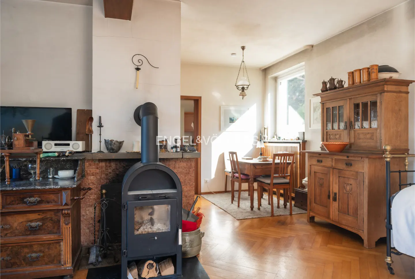 Living room with a black wood-burning stove, a dining table, and a wooden cabinet on a herringbone wood floor.