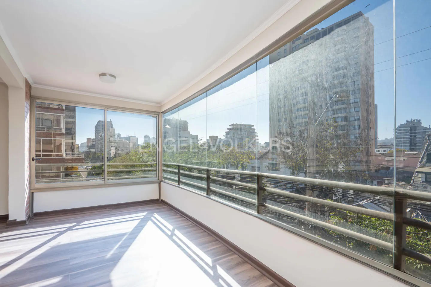 Bright sunroom with wood floors, glass walls, and a city view. Metal railing outside.