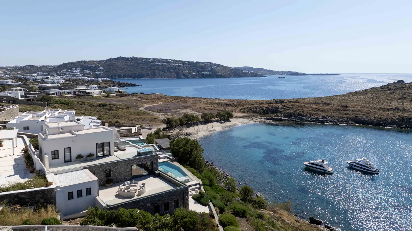 Aerial view of a white villa with a pool overlooking a bay with two yachts.