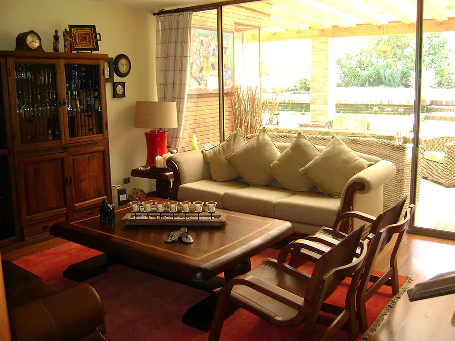 Living room with a wooden cabinet, sofa with pillows, coffee table with cups, and chairs on a red rug.