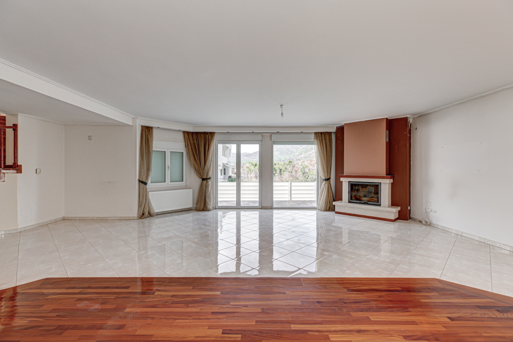 Bright, empty living room with tile floors, fireplace, and large windows with curtains.