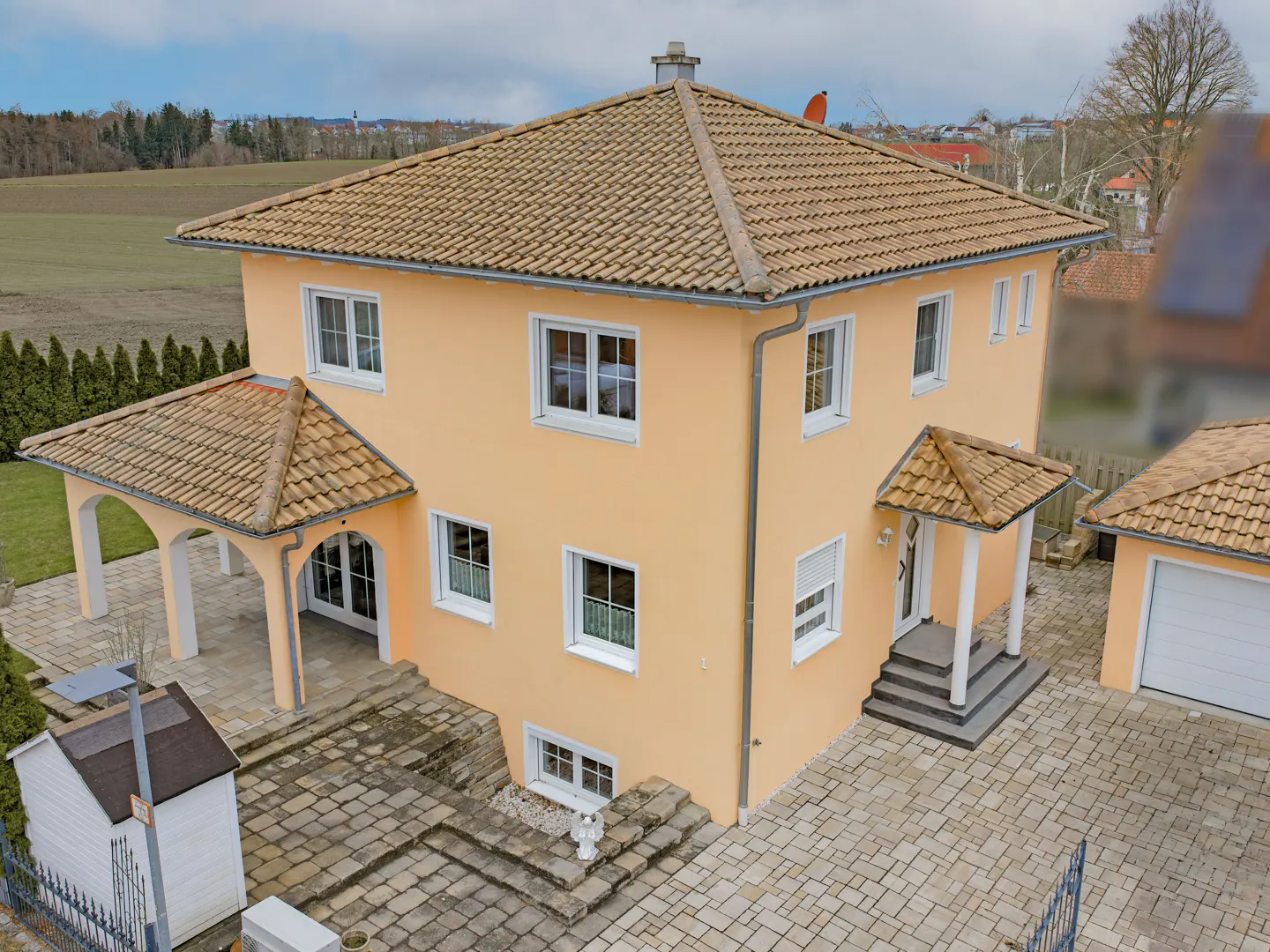 Two-story peach house with a tan tile roof and white trim. A stone patio and green lawn surround the home.