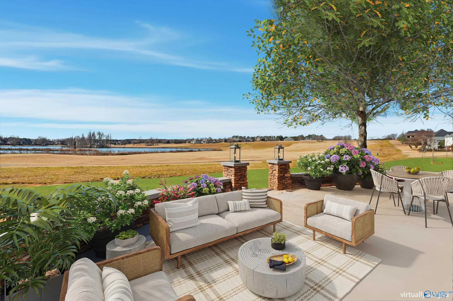 Outdoor patio with gray sofa, chairs, and table on a patterned rug. A green lawn and blue sky are in the background.