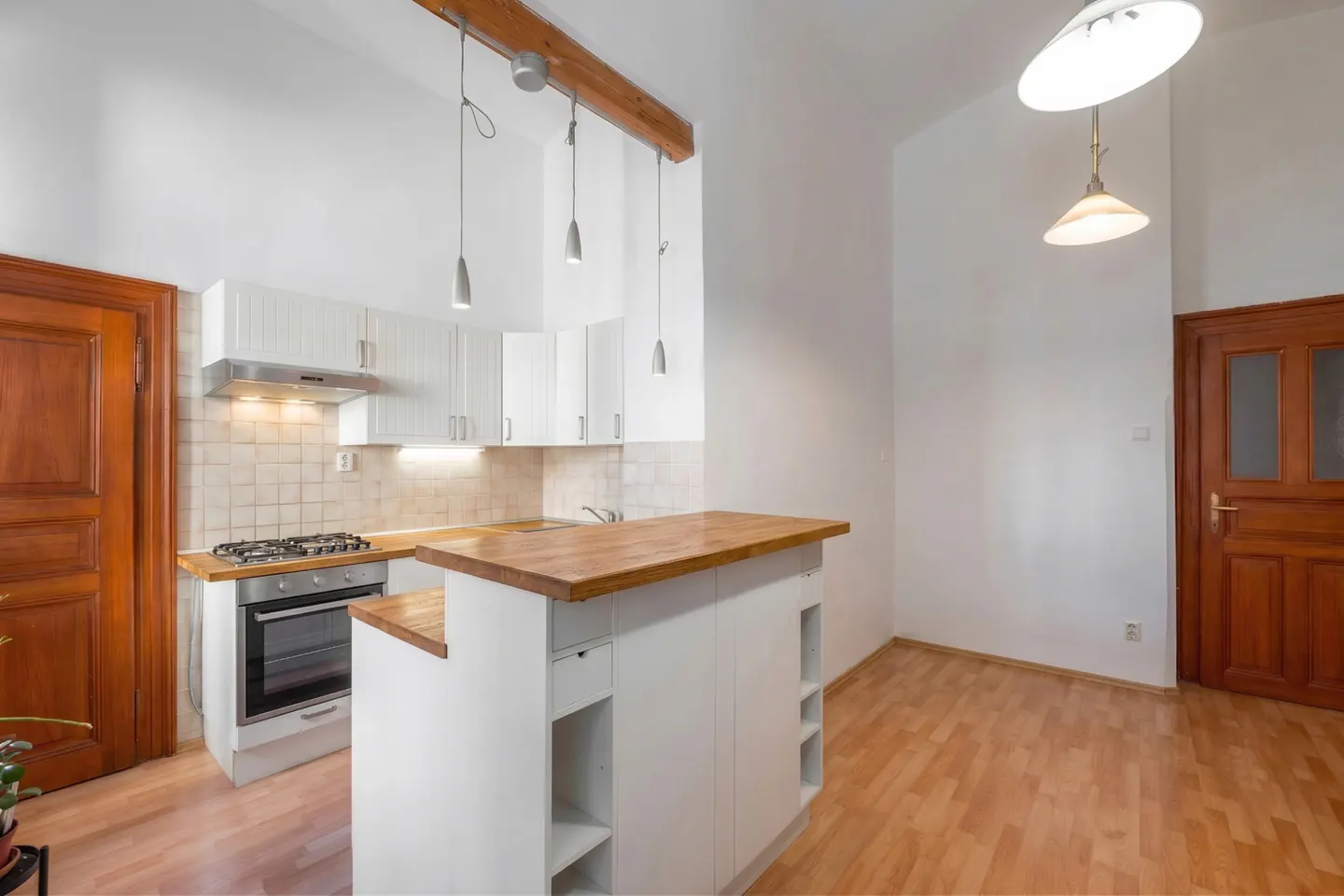 Modern kitchen with white cabinets, wooden countertops, a breakfast bar, and warm wood doors in a bright, open space.