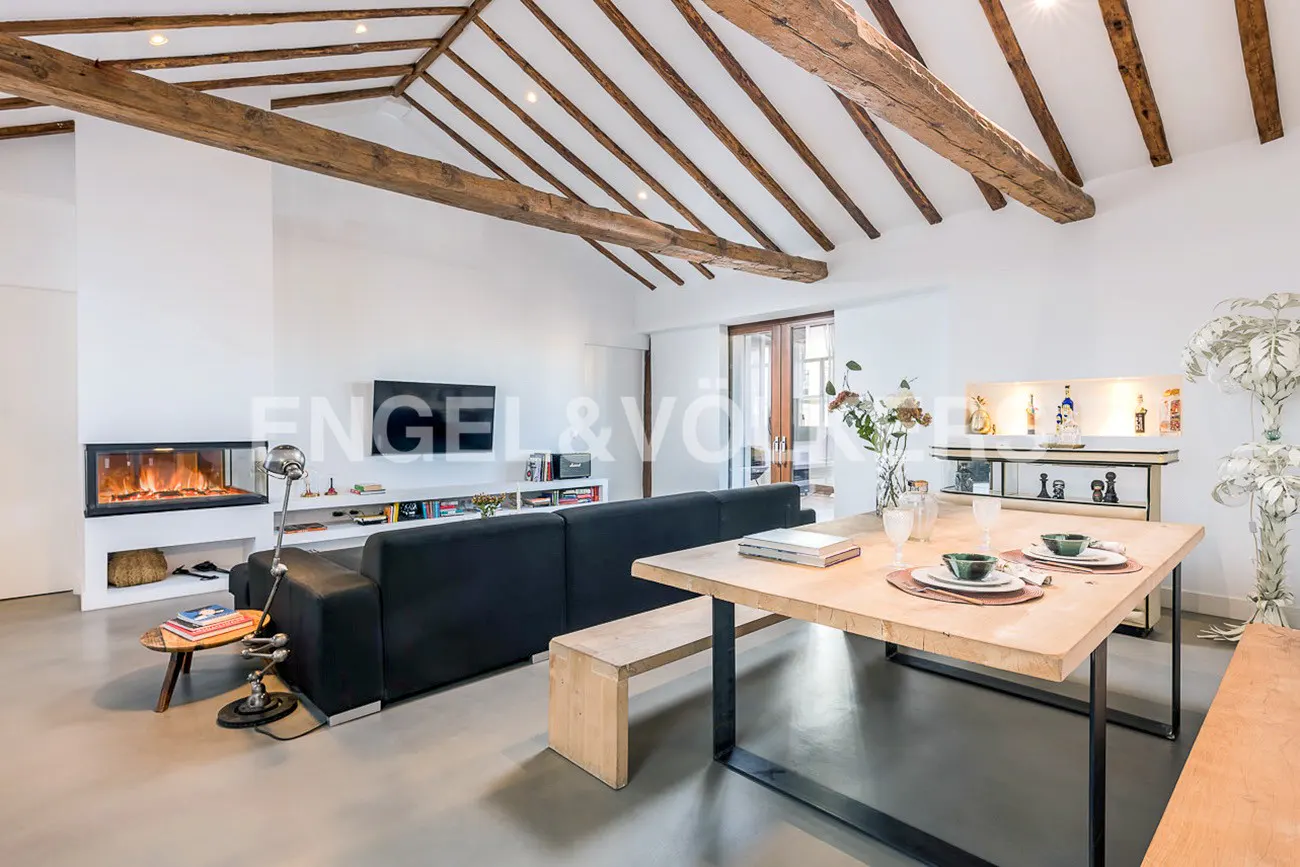 Bright living room with exposed wood beams, a black sofa, a fireplace, and a dining table set for two.