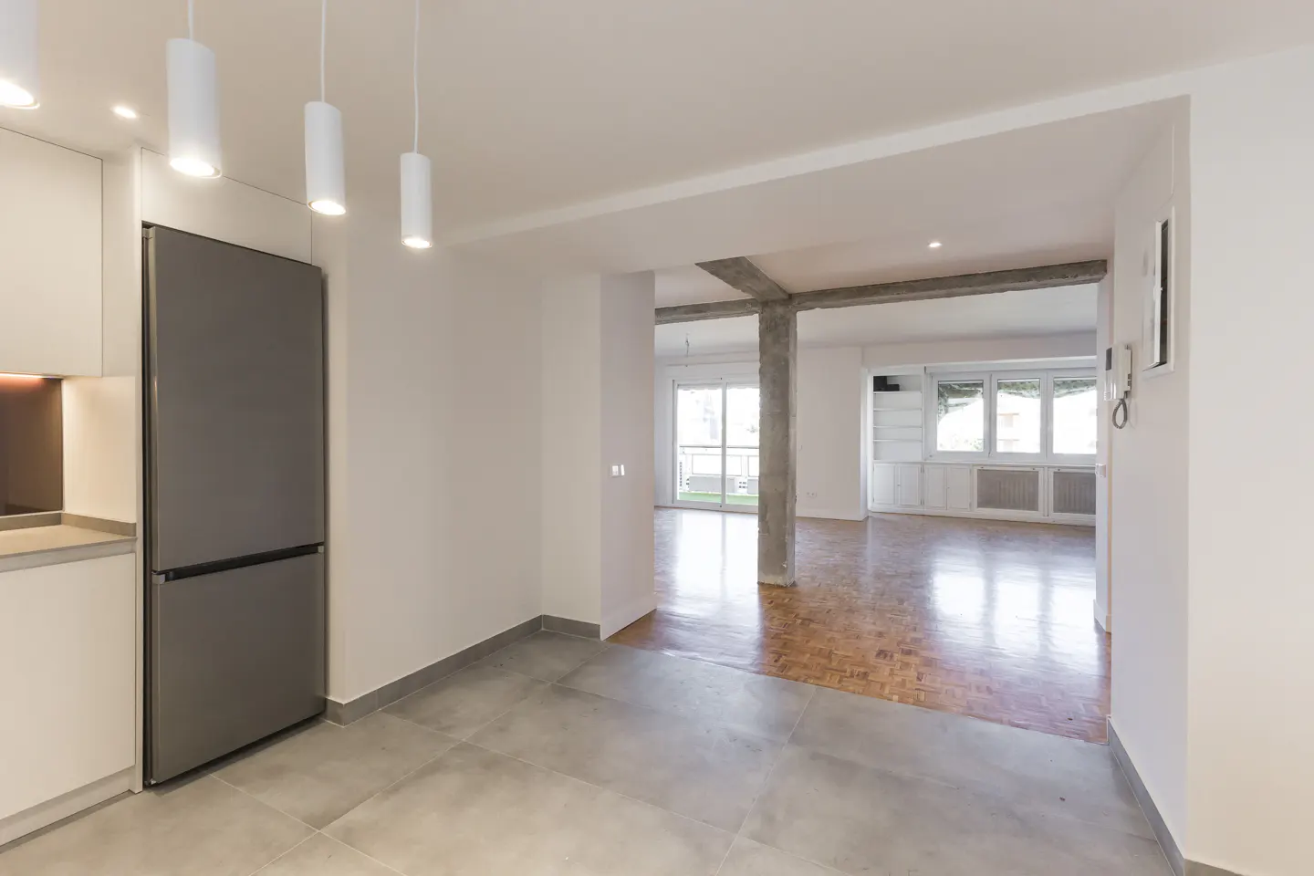 Modern kitchen with stainless steel fridge and pendant lights, opening into a spacious living area with parquet flooring.