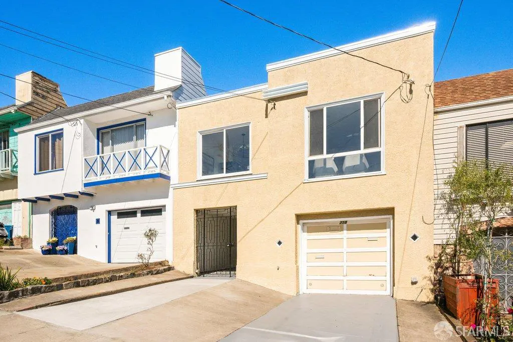 Exterior view of a beige two-story home with a white garage door, next to a white house with a blue balcony under blue sky.