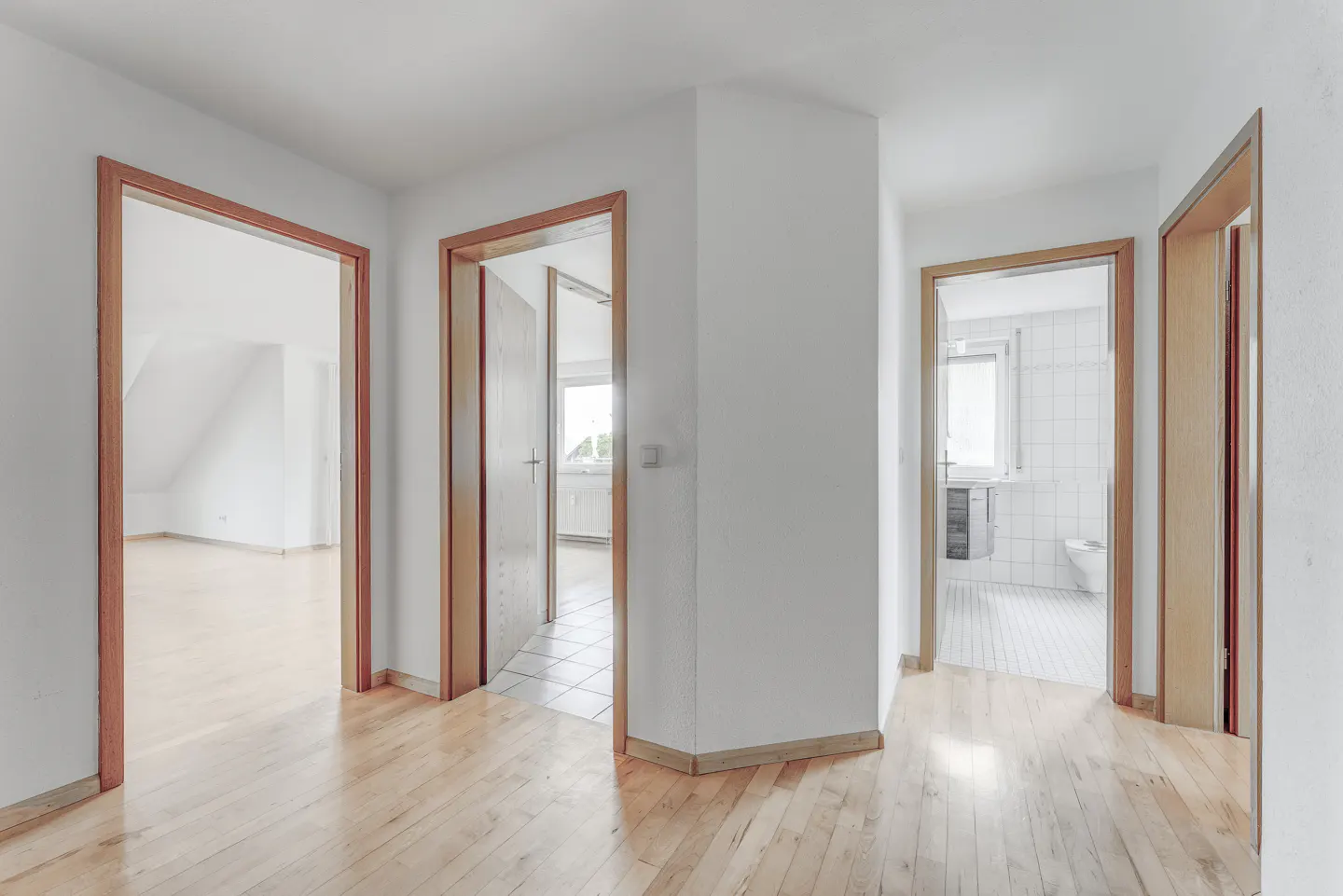 Hallway with light wood floors, white walls, and three open wood-framed doorways leading to other rooms.