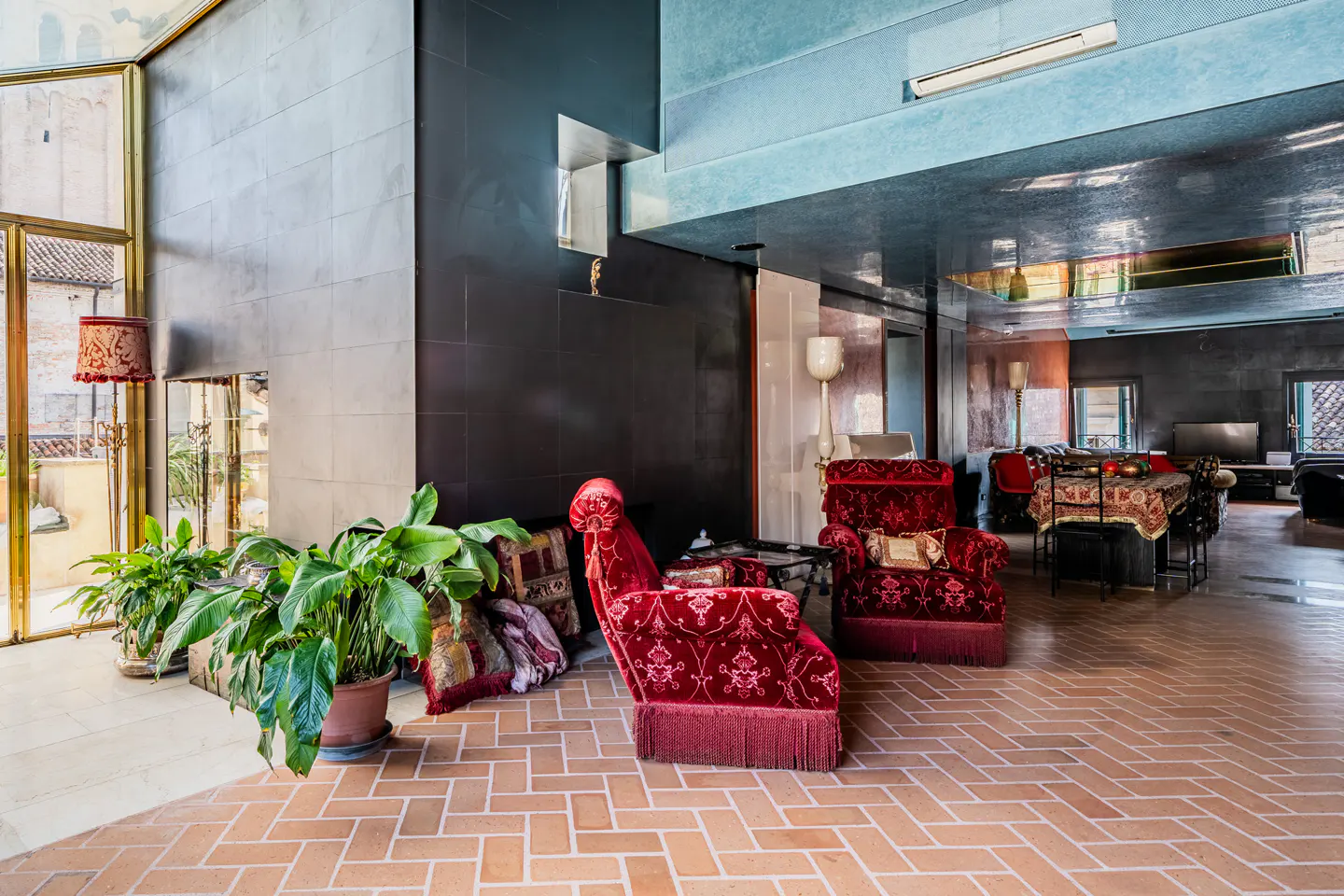 A living room with red velvet chairs, plants, and a brick floor.