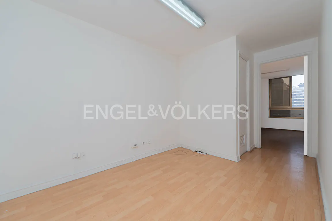 Empty room with white walls, light wood flooring, a fluorescent ceiling light, and a doorway leading to another room.