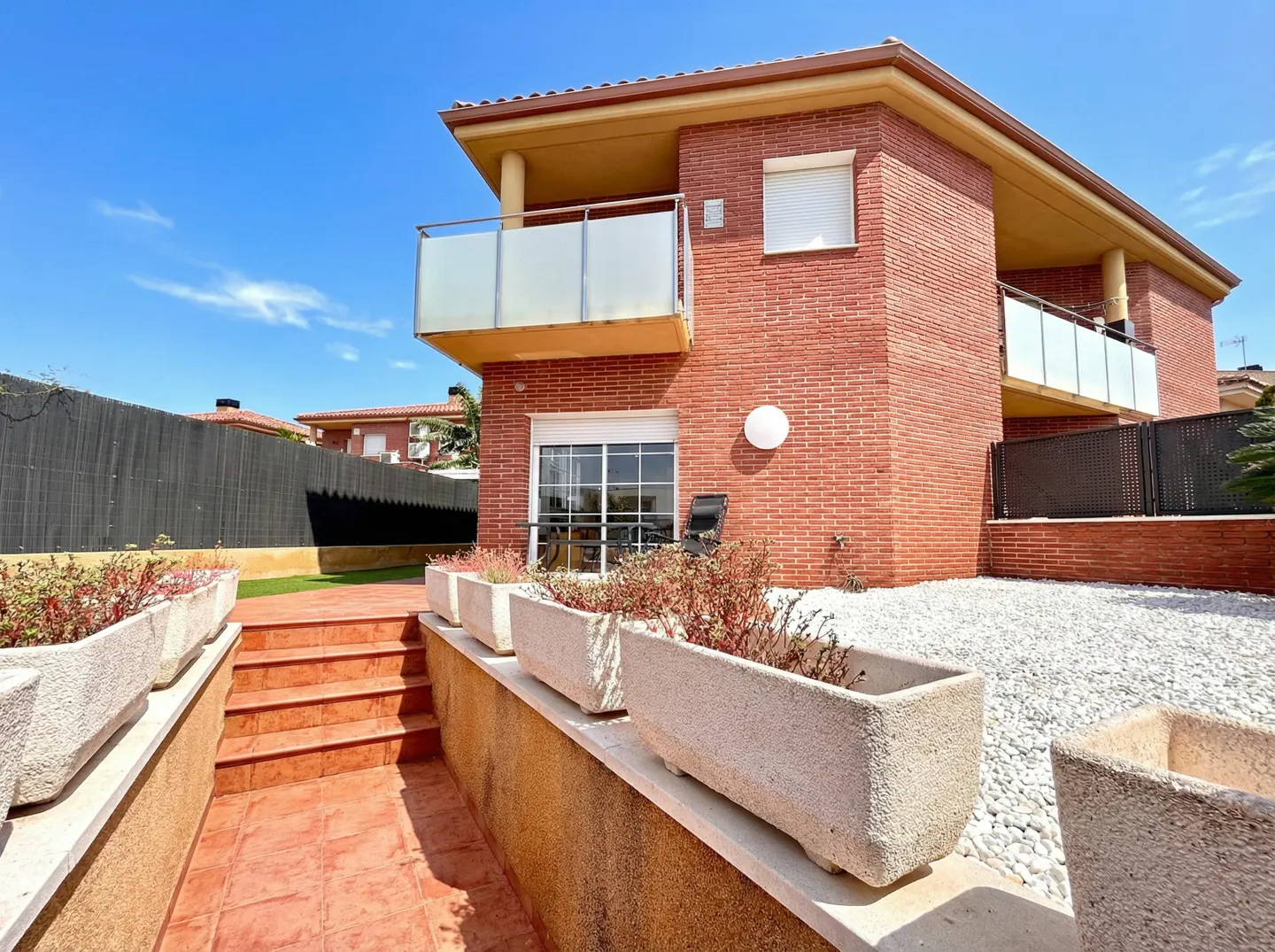 Brick house with a balcony, white gravel, and planter boxes under a blue sky.