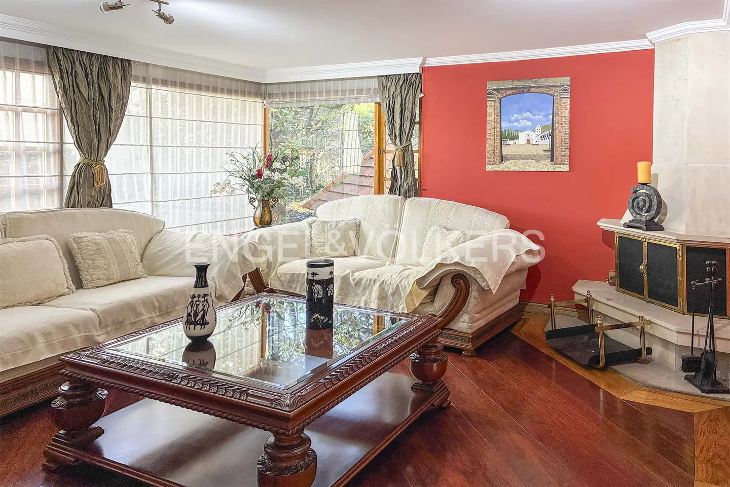 Living room with white sofas, a dark wood coffee table, and a bright red accent wall featuring a framed painting.