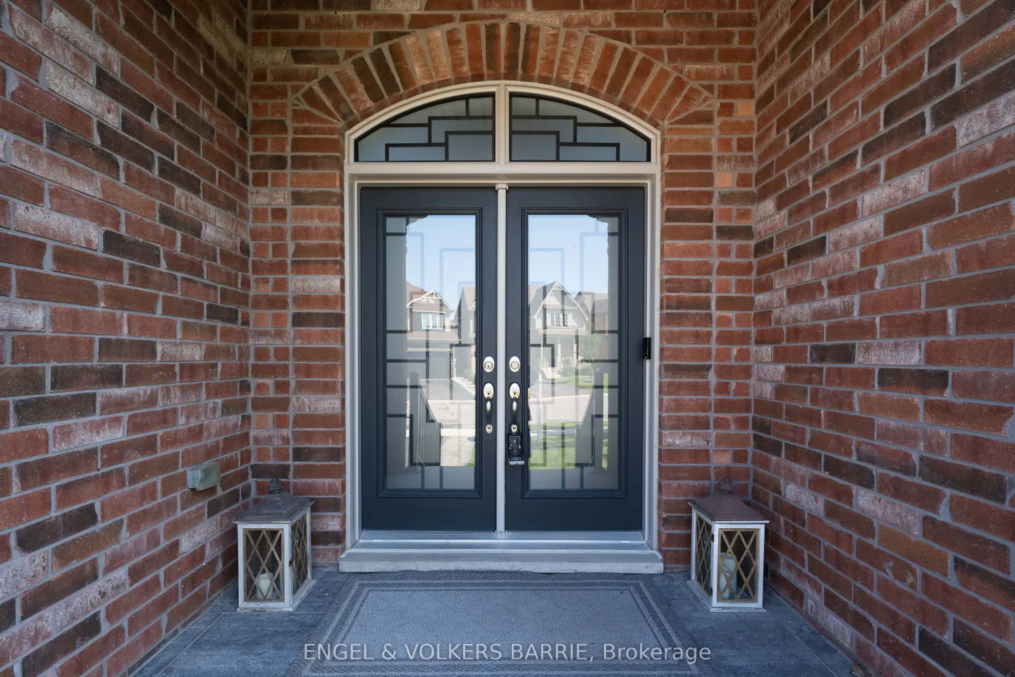 Exterior of a brick house with black double doors and decorative glass panels. Two lanterns flank the entrance.
