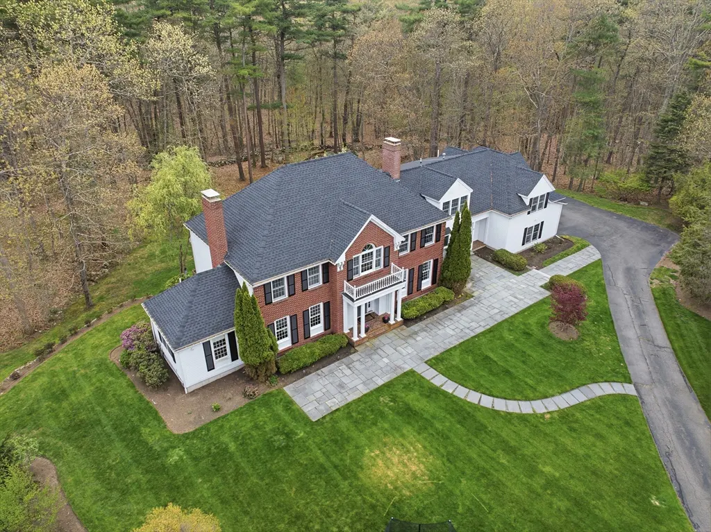 Aerial view of a large brick house with a gray roof, white trim, and a green lawn surrounded by trees.