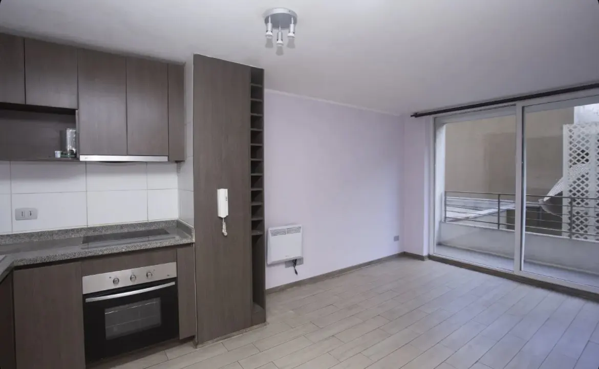 A modern apartment interior with brown cabinets, oven, and a sliding glass door to a balcony.