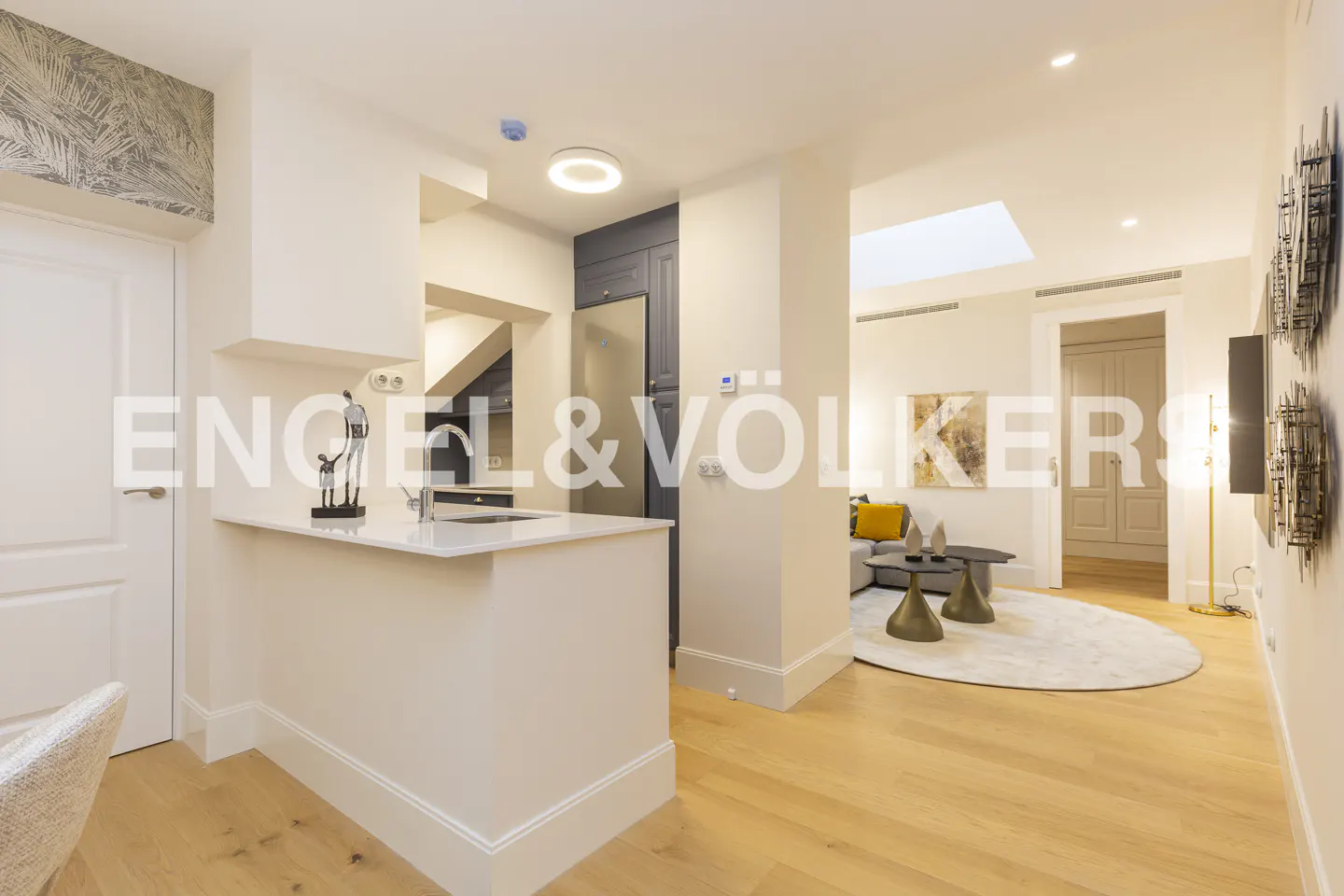 Modern kitchen with white island and dark cabinets, opening into a bright living room with light wood floors and a skylight.