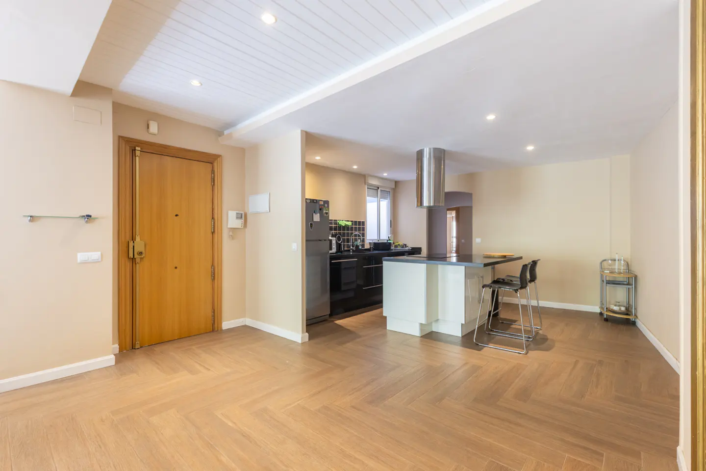 Open-concept apartment with herringbone wood floors, a kitchen with a breakfast bar, and a wooden front door.