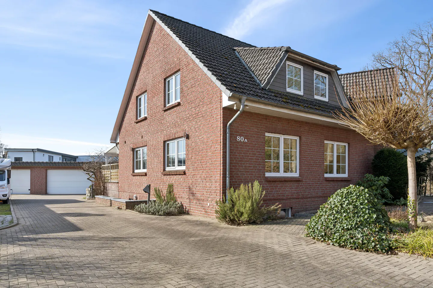 Red brick house with a dark tiled roof, white-framed windows, and a paved driveway leading to a double garage.