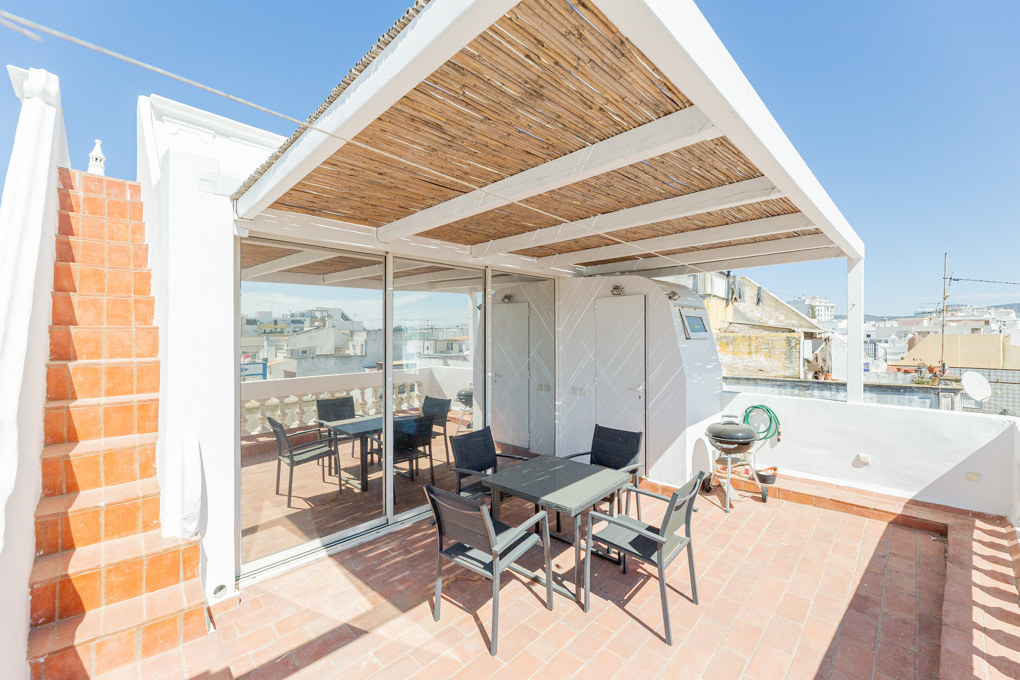 Sunny rooftop terrace with terracotta tiles, a bamboo-covered pergola, outdoor dining set, and city views.