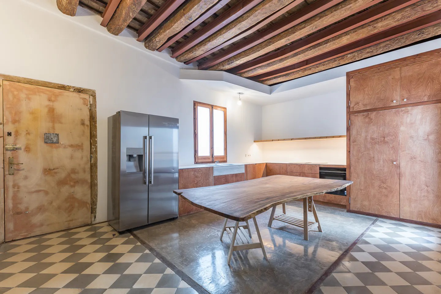 A kitchen with a stainless steel refrigerator, a wooden table, and a checkered floor.