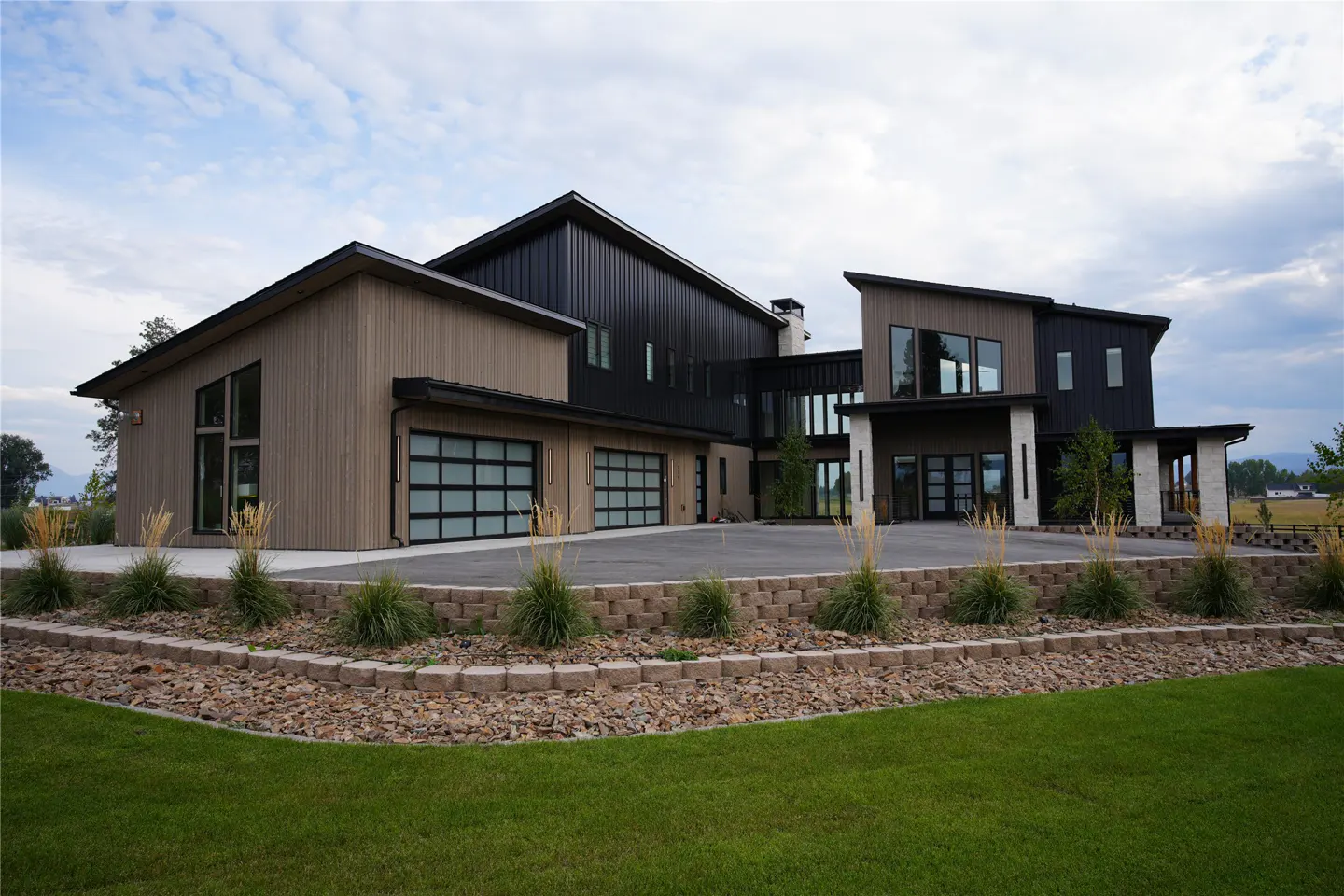 Modern two-story home with a two-car garage, brown and black siding, and a well-manicured lawn.