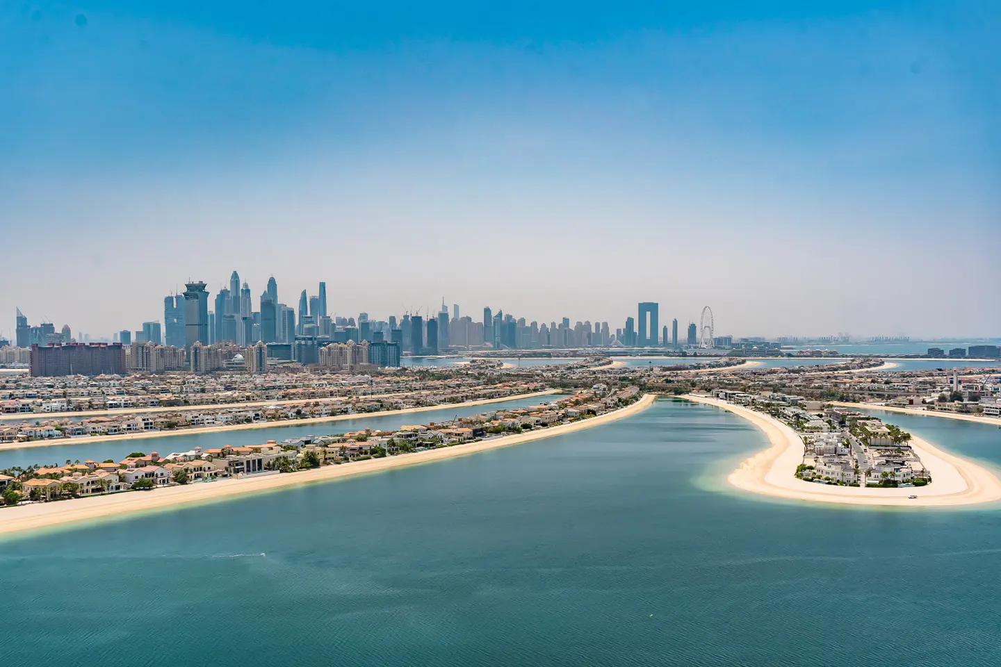 Dubai's Palm Jumeirah, an artificial archipelago, with luxury homes, sandy beaches, and the city skyline in the background under a clear blue sky.