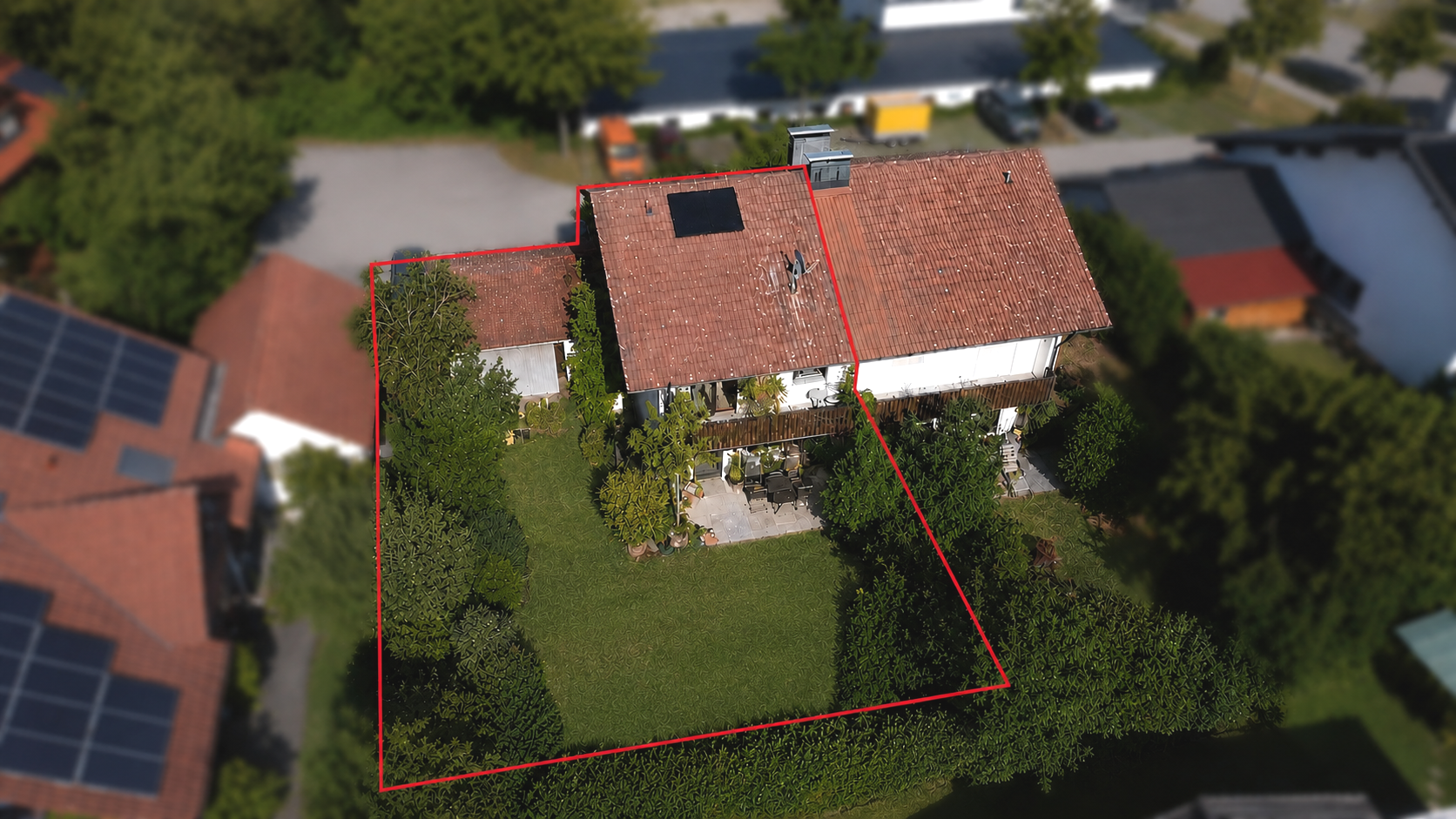 Aerial view of a house with a red-tiled roof and a large, fenced-in green backyard surrounded by trees and shrubs.