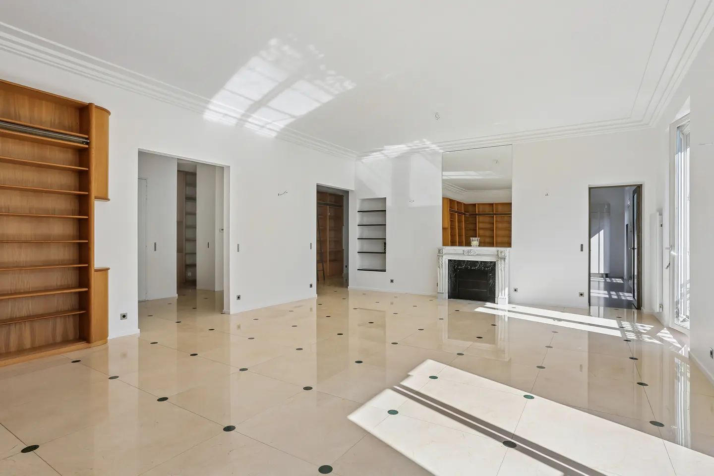 Bright, empty room with white walls, marble floors, and a fireplace. A large wooden bookcase stands against one wall.