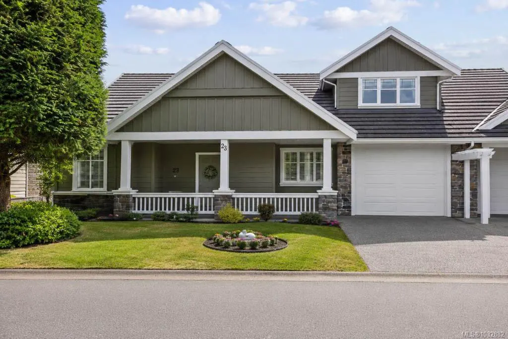 Single-story olive green house with a white porch, stone accents, a two-car garage, and a manicured front lawn.