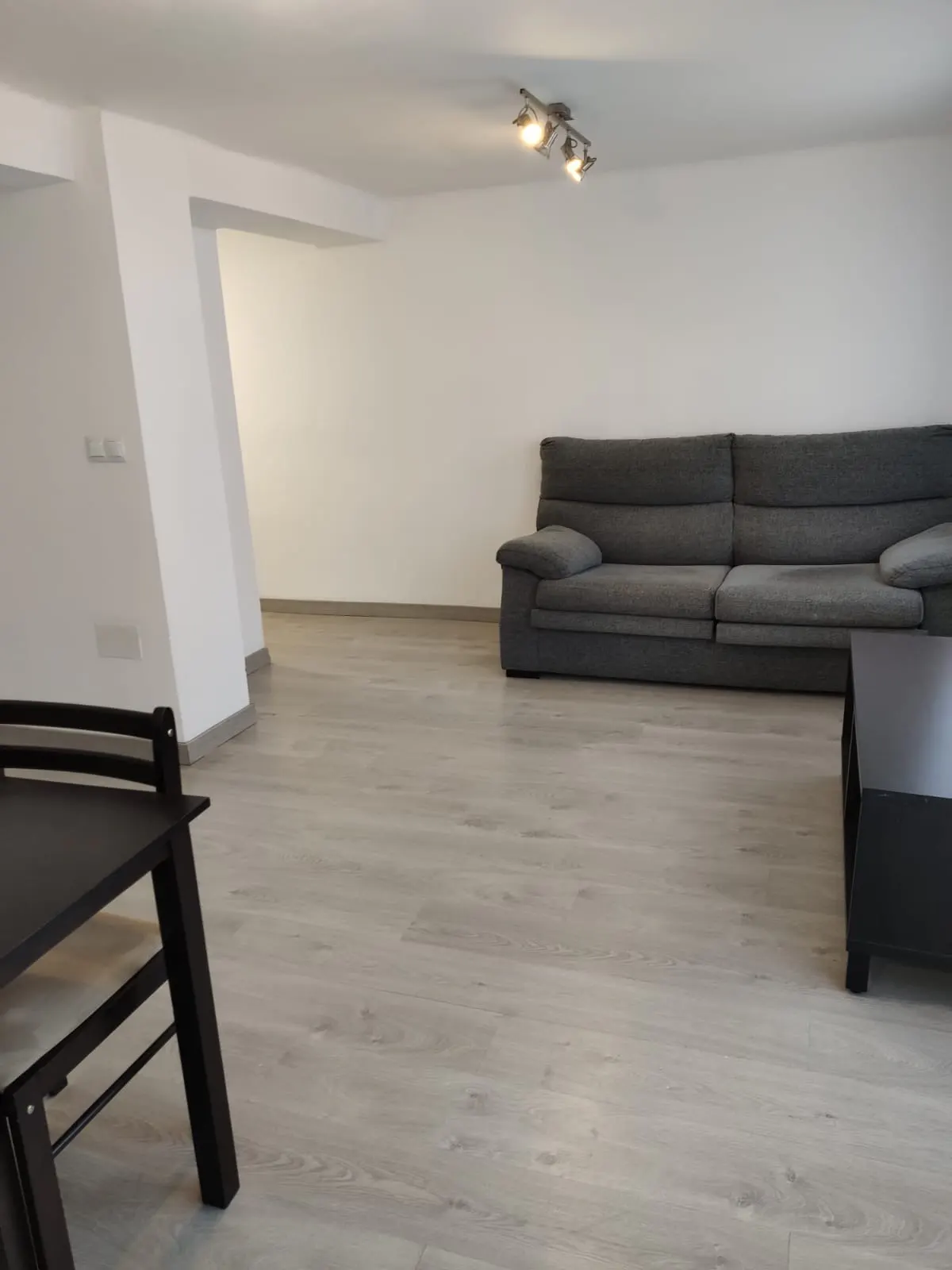 Minimalist living room with light wood floors, a large grey sofa, and a dark wood dining table in the foreground.