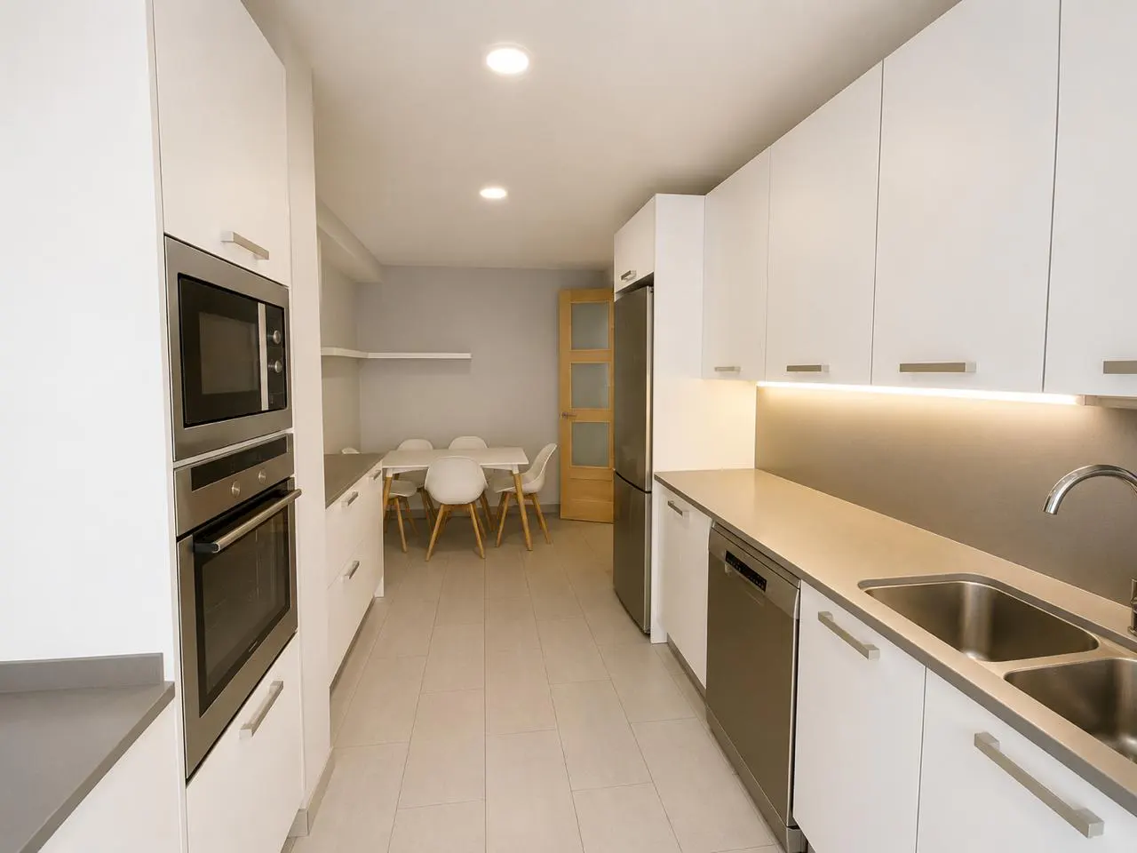 Bright, modern kitchen with white cabinets, stainless steel appliances, and a dining area with a white table and chairs.