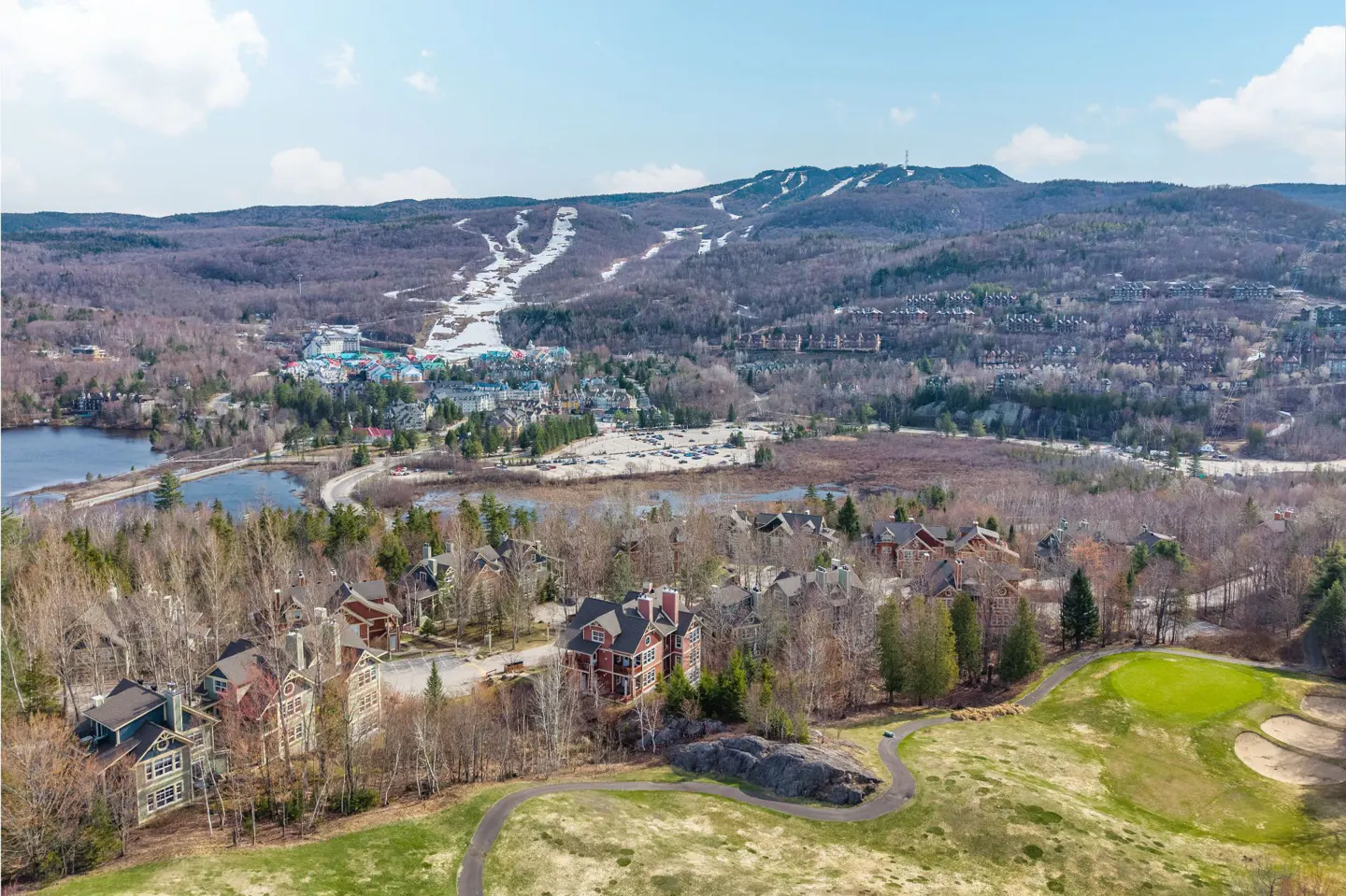 Aerial view of a ski resort town with a golf course in the foreground and ski slopes on a mountain in the background.