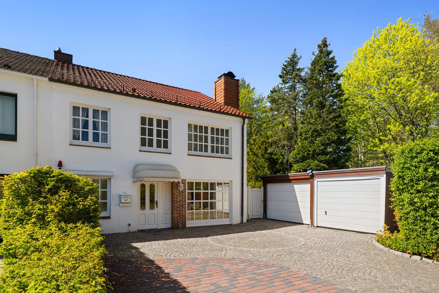 Two-story white house with a red tile roof, white garage doors, and a circular cobblestone driveway.