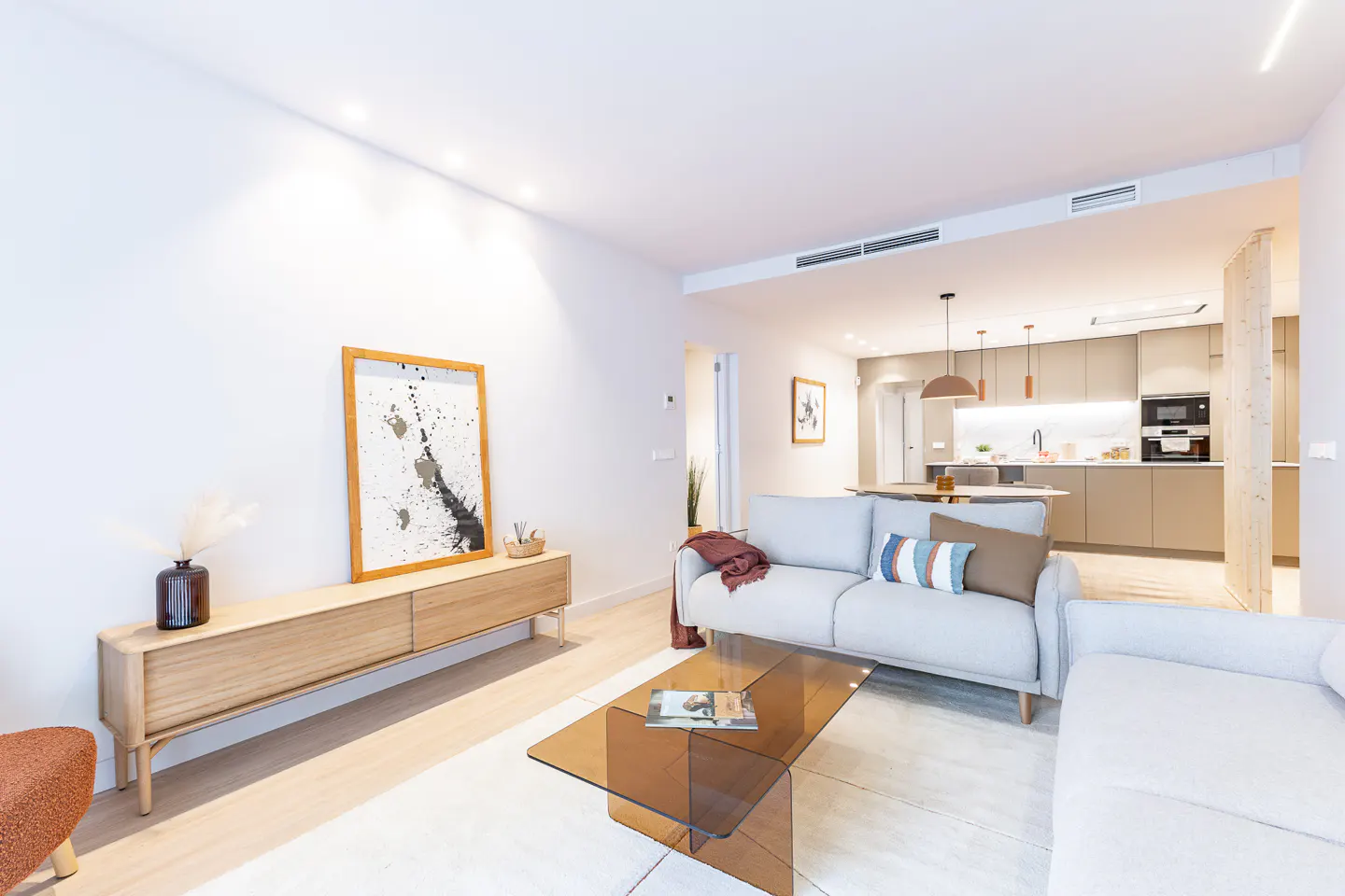 Modern living room with light gray sofas, a glass coffee table, and a wooden media console with abstract art.