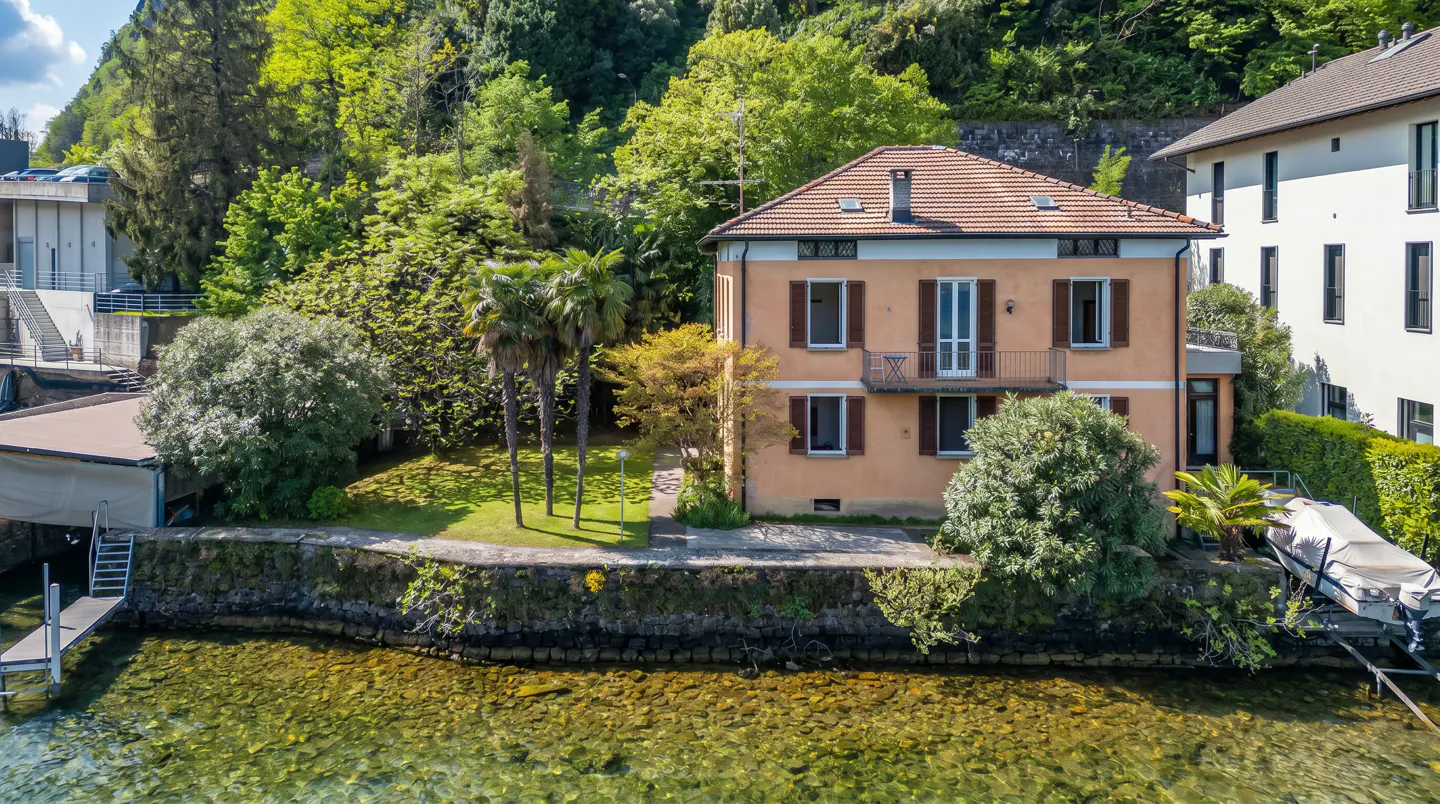 Two-story peach house with brown shutters and a red tile roof on a lakefront property with a boat dock.