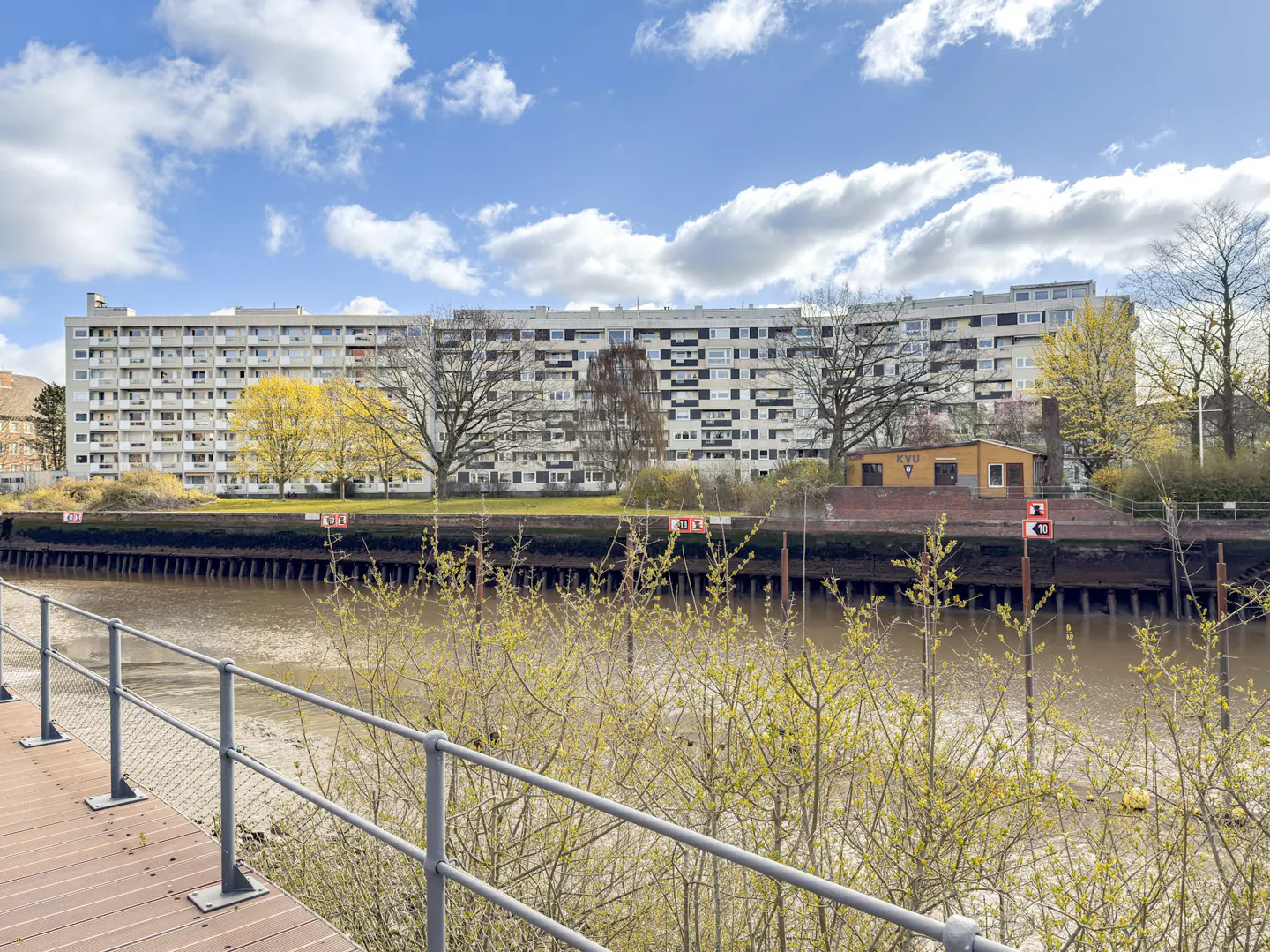 Apartment building on the Elbe river, Hamburg. Gray building with many windows, trees, and a small yellow house.