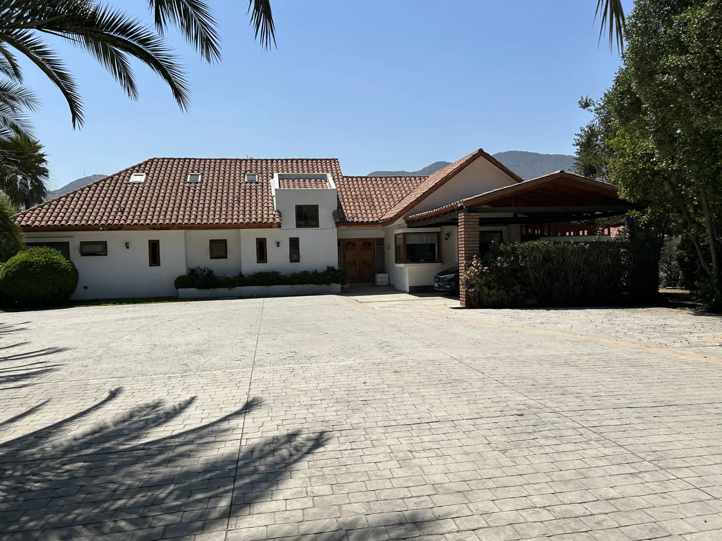 A white house with a red tile roof and a large paved driveway on a sunny day.