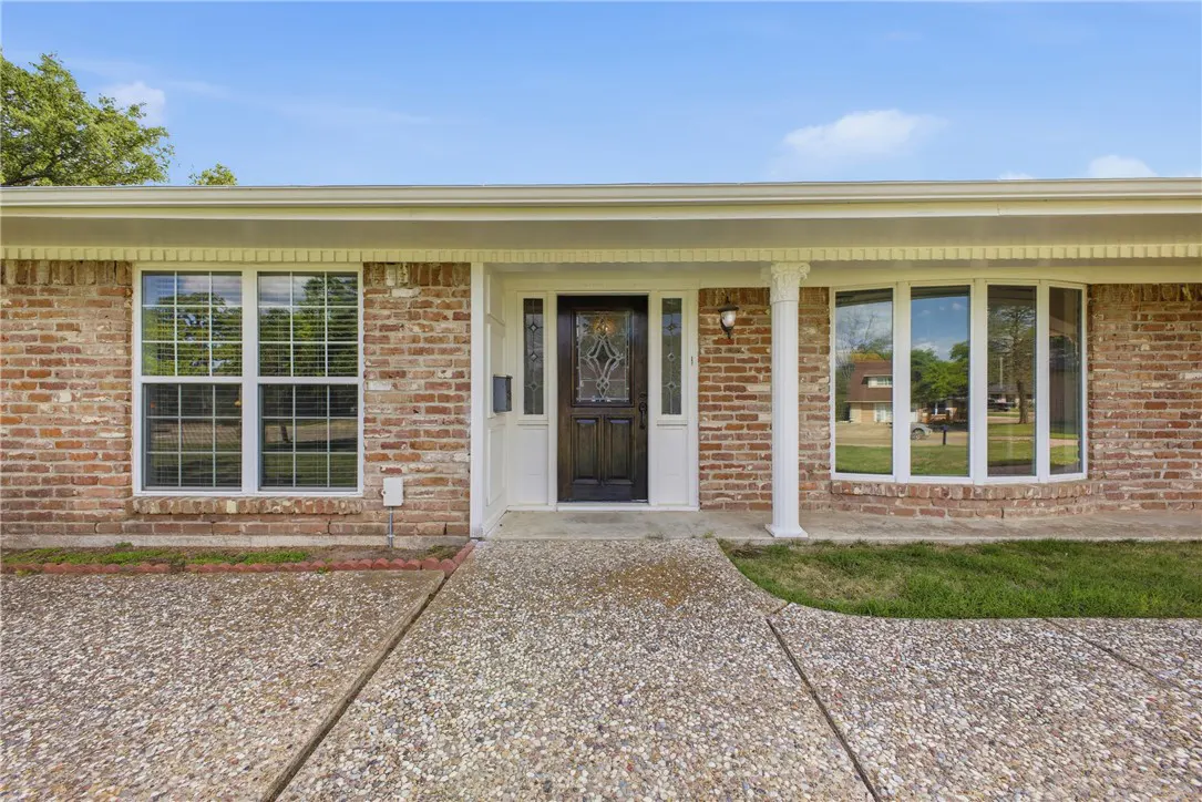 Front exterior of a brick home with a dark wood door, white trim, and a concrete walkway.
