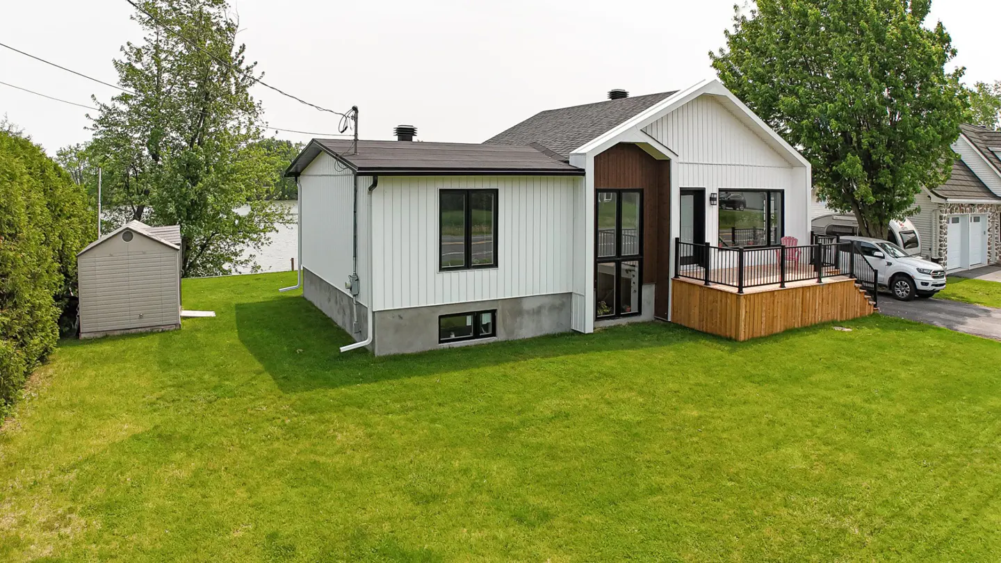A modern white house with a black roof and trim, a wooden deck, and a green lawn.