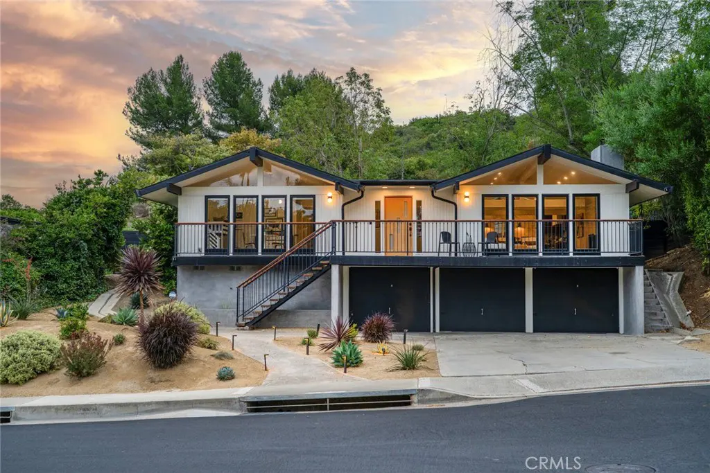 Modern mid-century home with white siding, black trim, a large balcony, and a three-car garage at sunset.