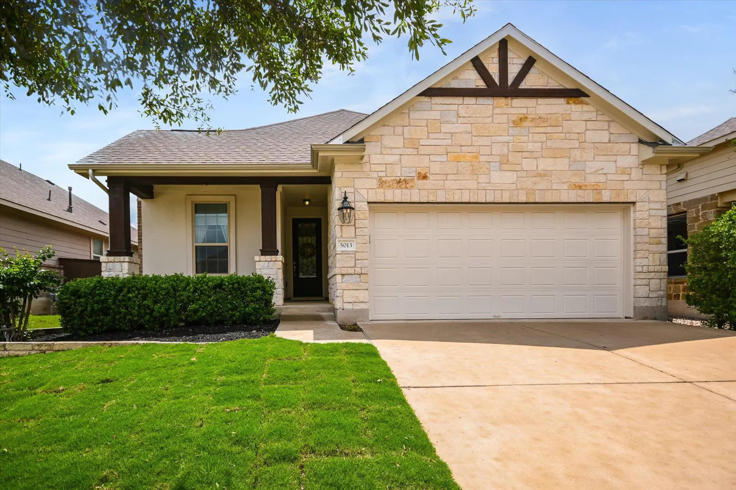 A single-story house with a stone facade, a two-car garage, and a well-manicured lawn.
