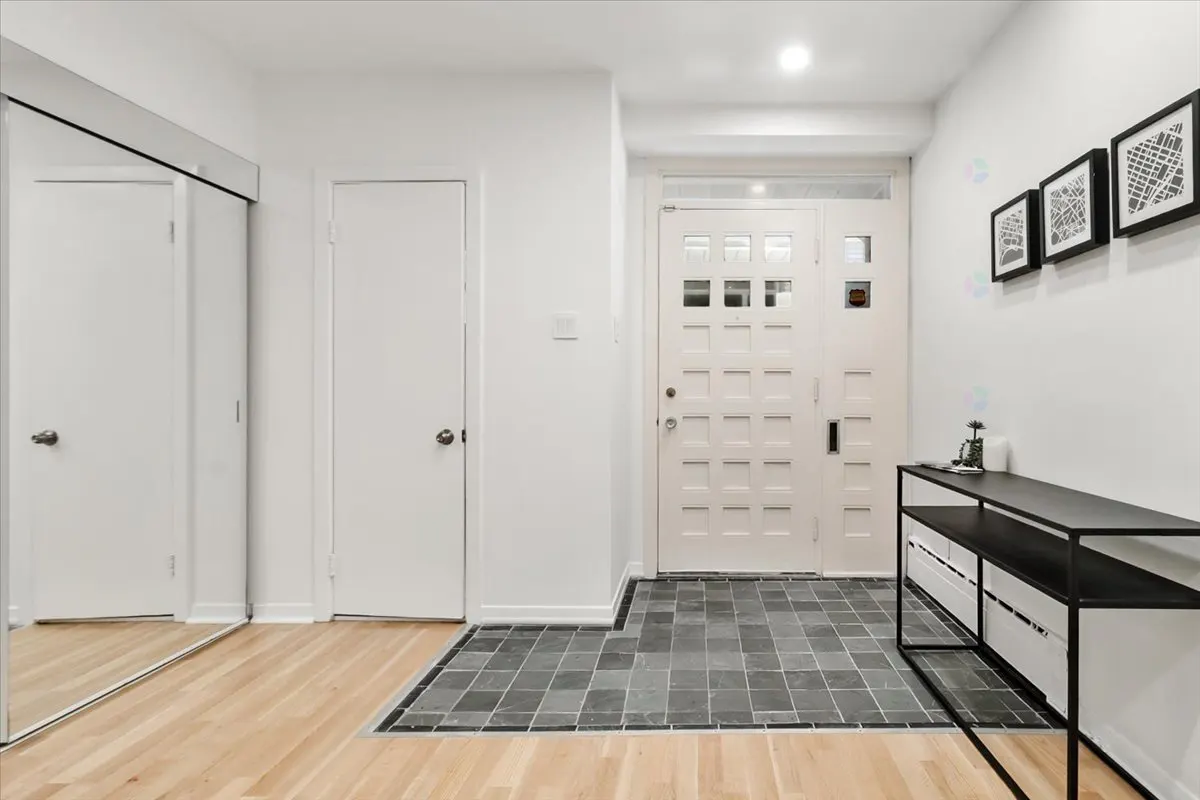 Bright entryway with light wood floors, a dark tiled foyer, white front door, mirrored closet, and black console table.