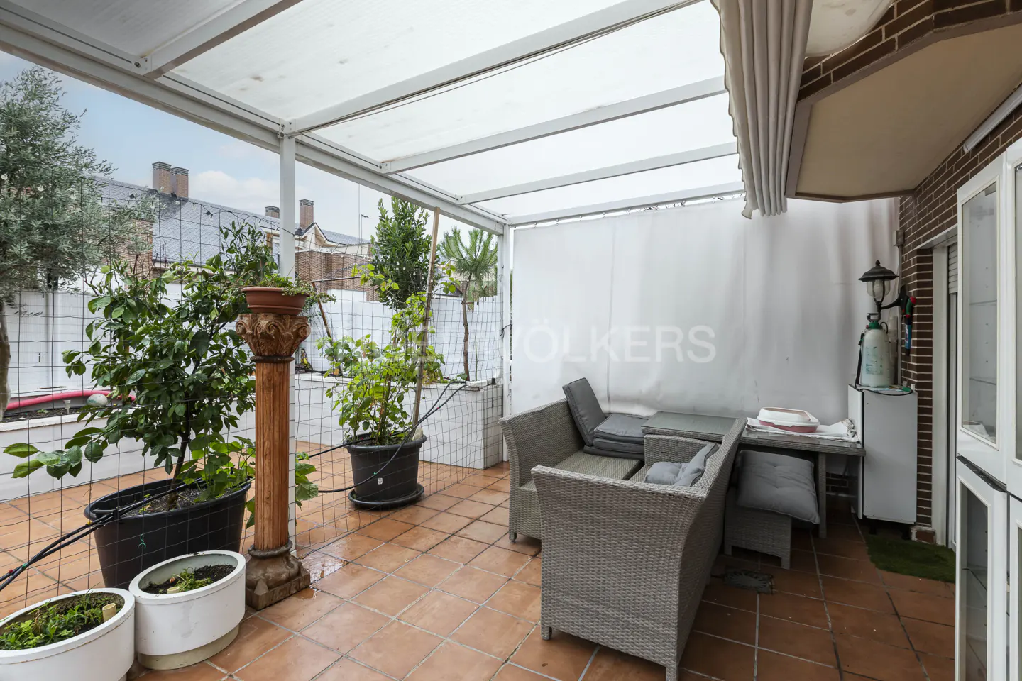 Covered terrace with terracotta tiles, grey wicker outdoor furniture, potted plants, and a decorative wooden pillar.
