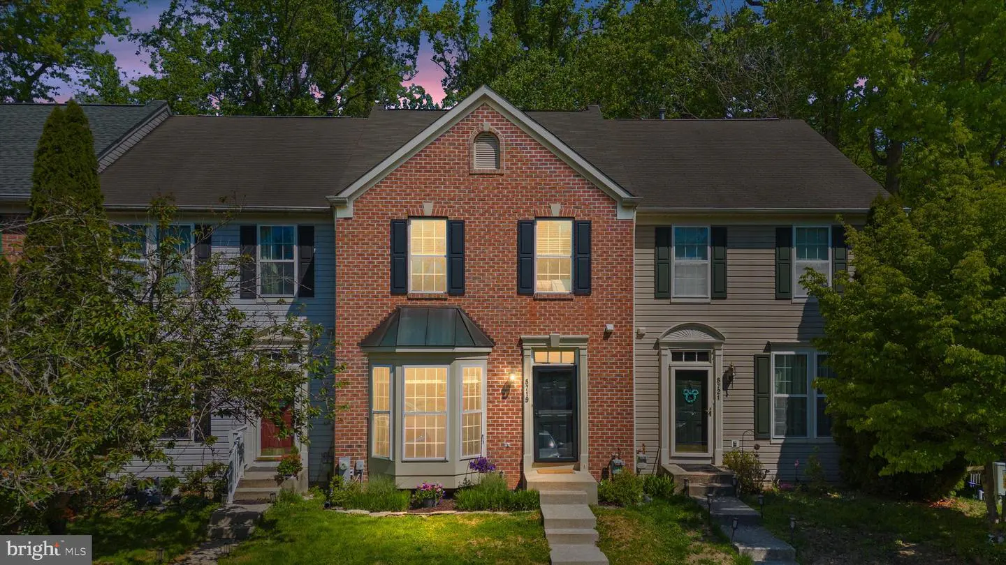 Exterior view of a brick townhouse with black shutters and a bay window, flanked by two similar townhouses.