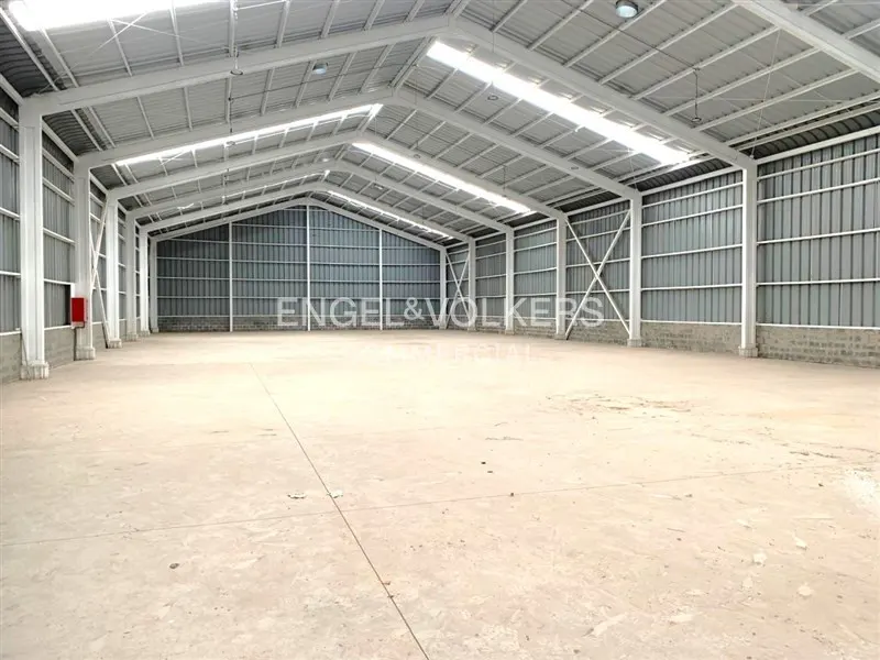 A large, empty warehouse with a concrete floor, metal walls, and a white steel frame.
