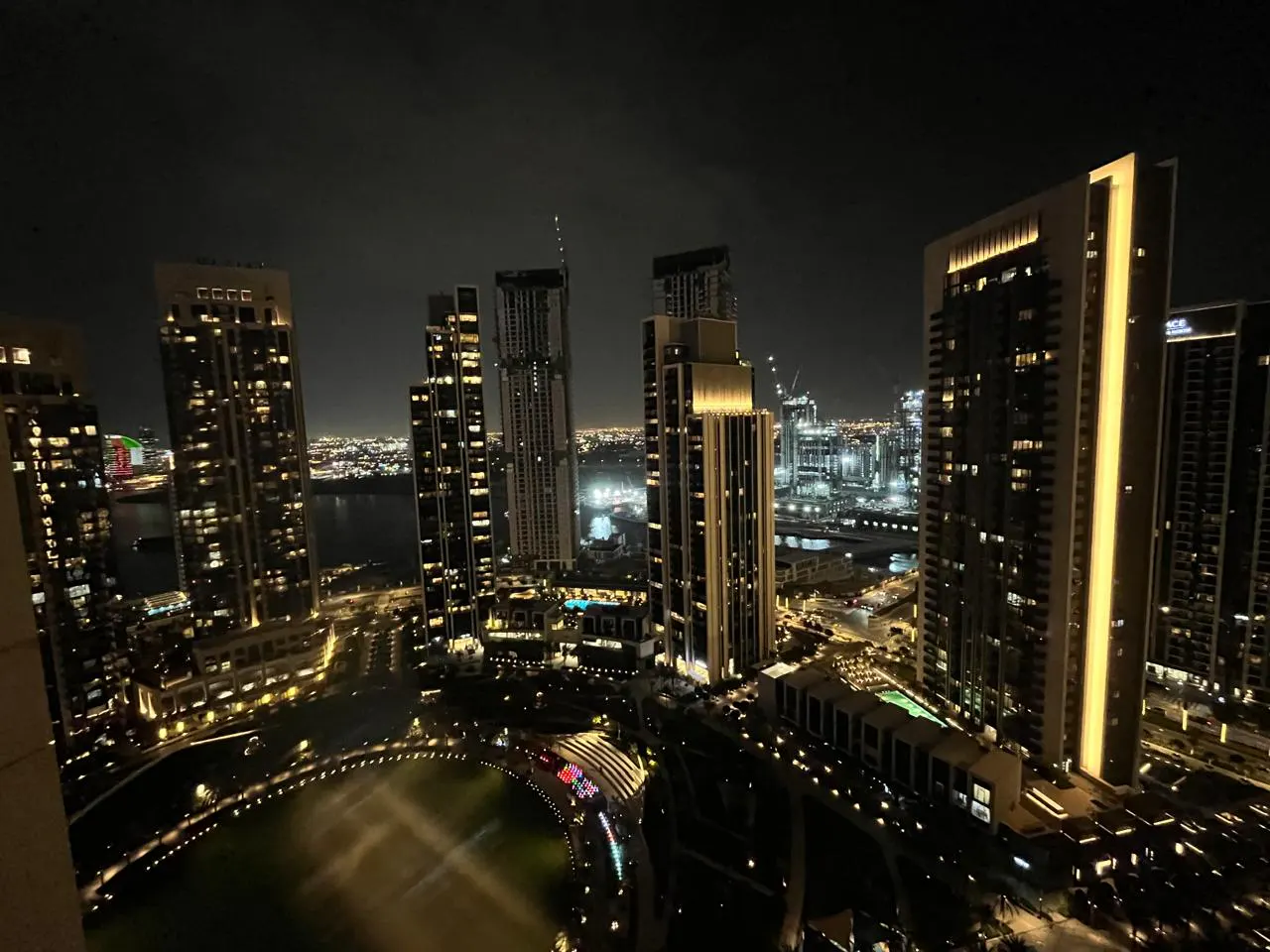 Night view of Dubai skyline featuring illuminated skyscrapers, a green park, and city lights.
