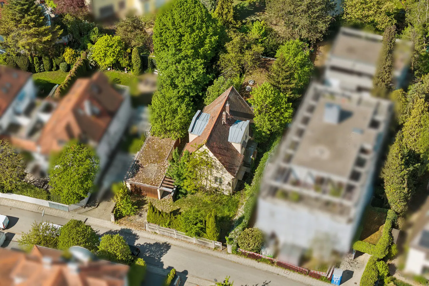 Aerial view of a house with a red tile roof surrounded by green trees and other houses in a suburban neighborhood.