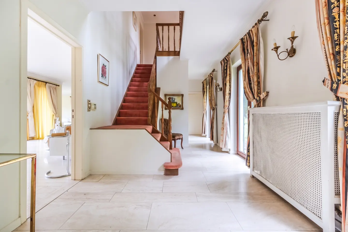 Bright foyer with marble floors, a red-carpeted staircase, and patterned curtains by glass doors. A white radiator sits against the wall.