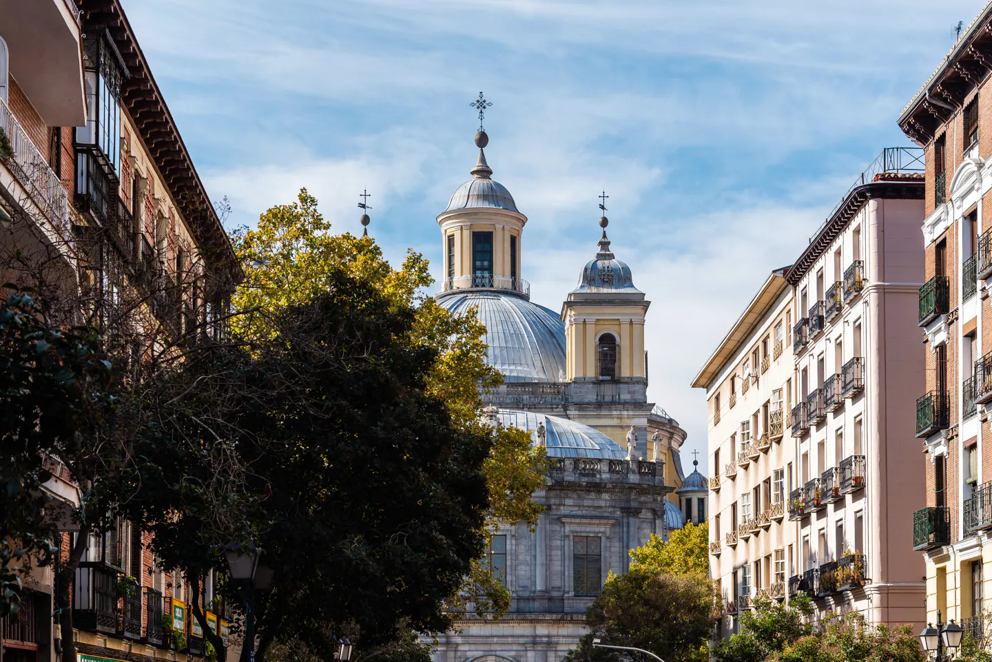 A close-up of colorful residential buildings with decorative balconies next to an ornate market building. The market features a mosaic-style façade with stained glass windows and an arched entrance, all under a partly cloudy sky.